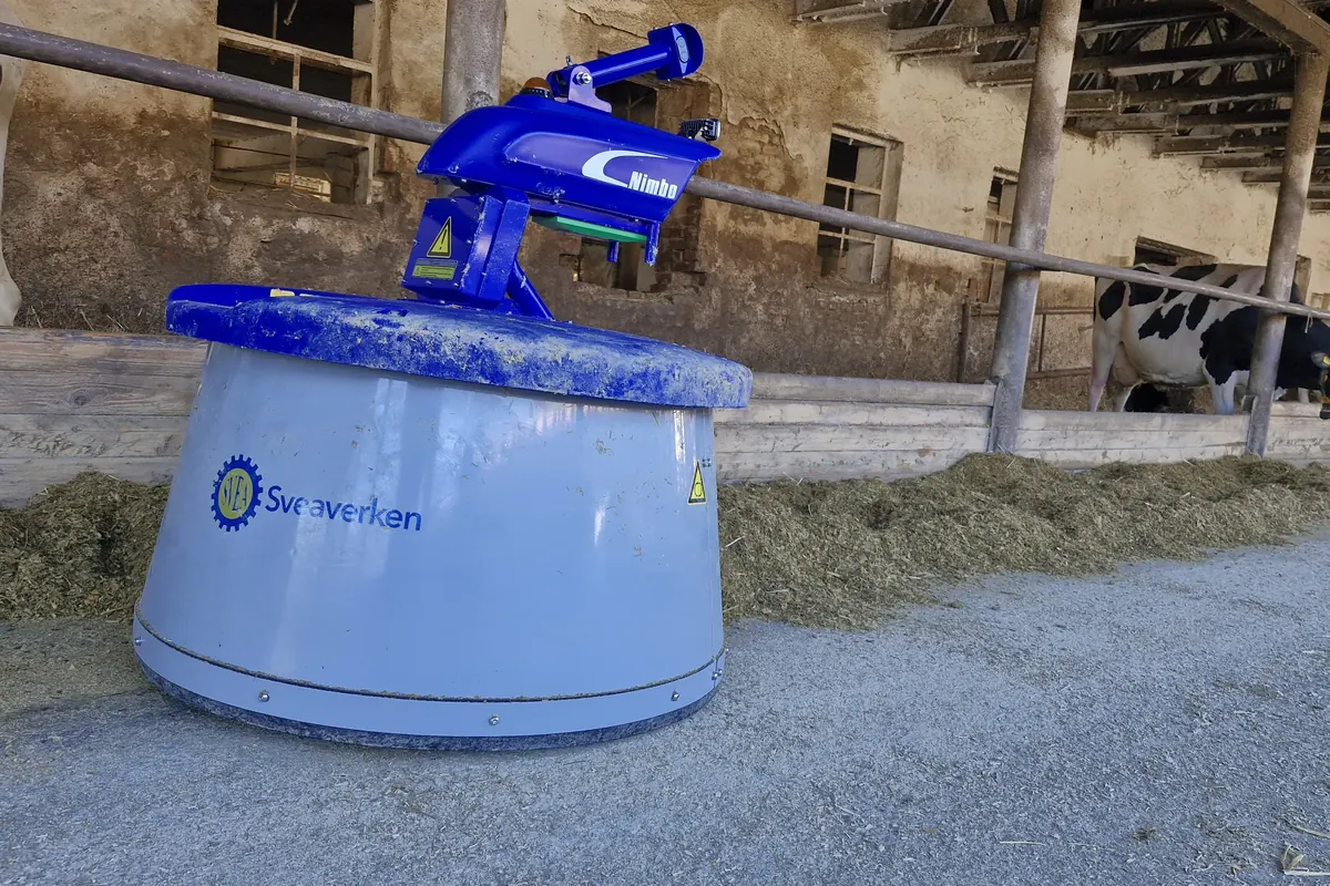 Robot Nimbo s modrým krytem na krmné chodbě posypané krmivem