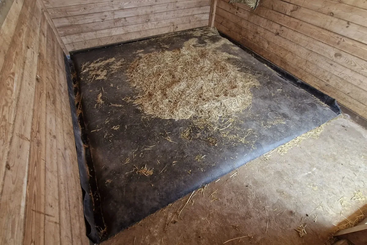 Pryžová matrace na podlaze koňského boxu s dřevěným obložením a slámou
