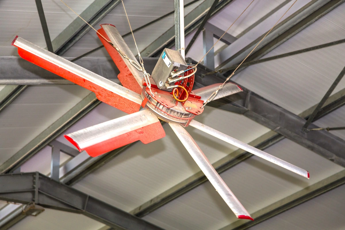 Velkoprůměrový ventilátor s hliníkovými lopatkami zavěšený pod ocelovou konstrukcí haly