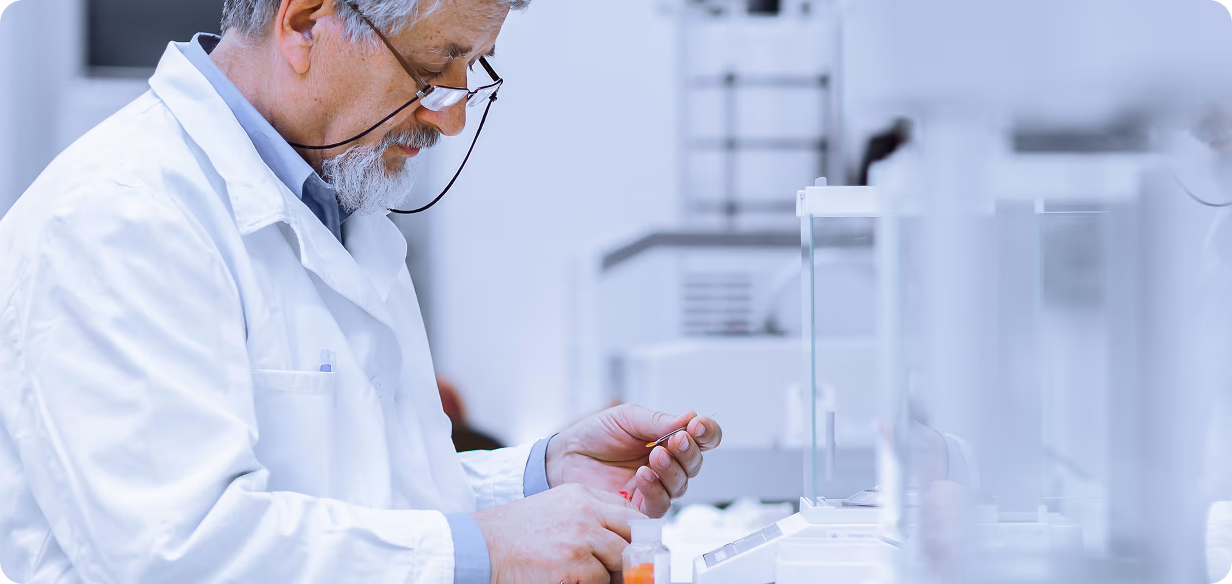 Scientist in a white lab coat examining a small object in a bright laboratory setting.