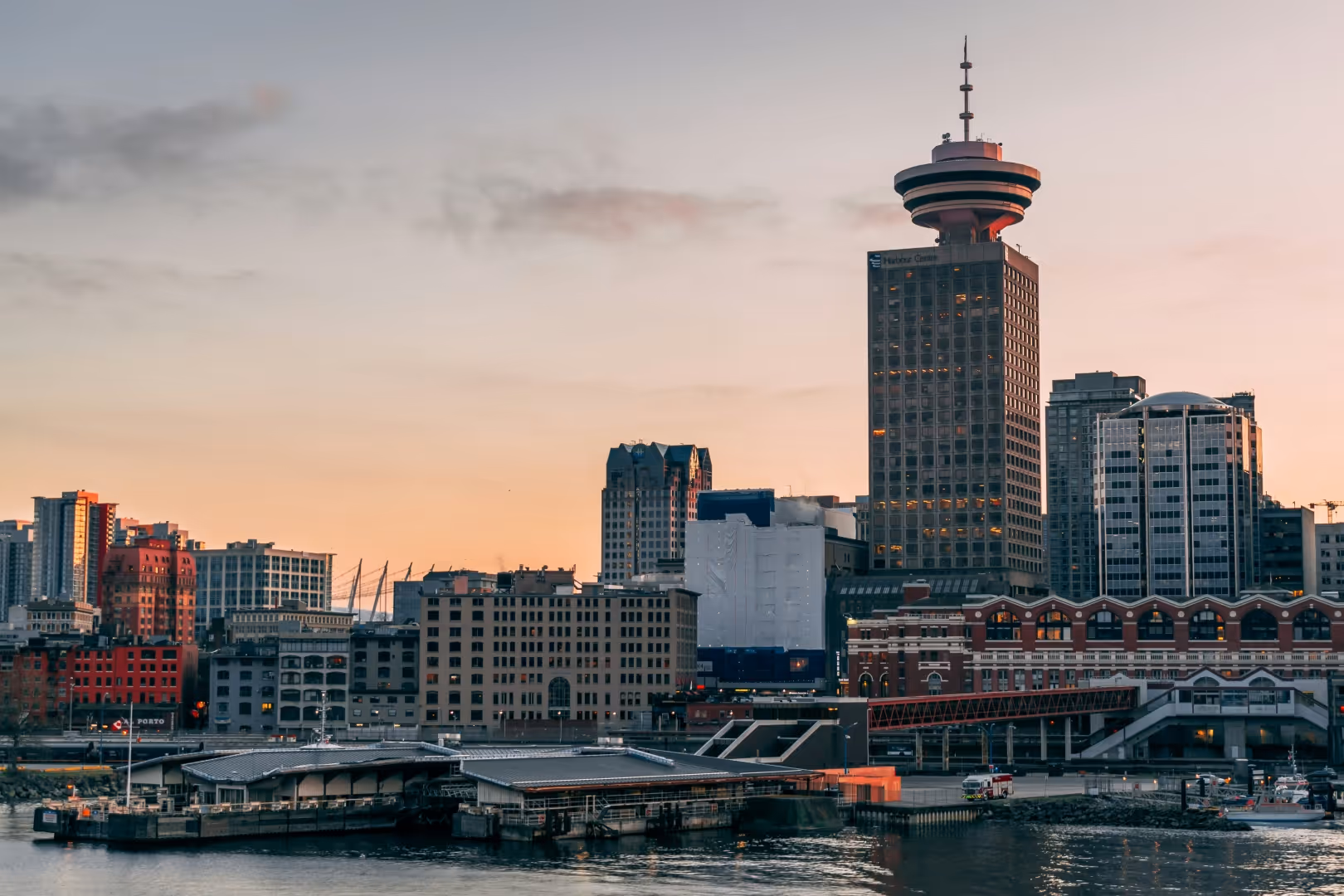 Vancouver skyline at sunset with Harbour Centre tower and waterfront buildings along the harbor.