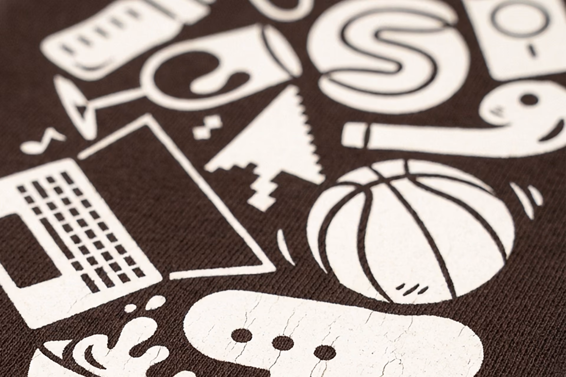 Close-up of white icons on brown fabric, including a basketball, laptop, and speech bubble.