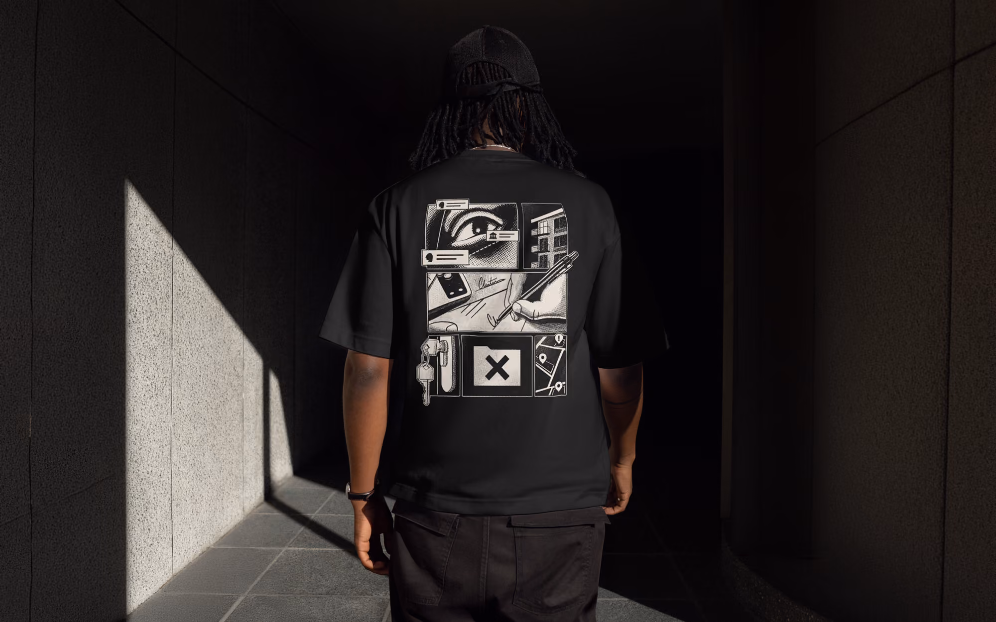 Person wearing black T-shirt with graphic panels showing an eye, building, hand signing, keys, and a map.