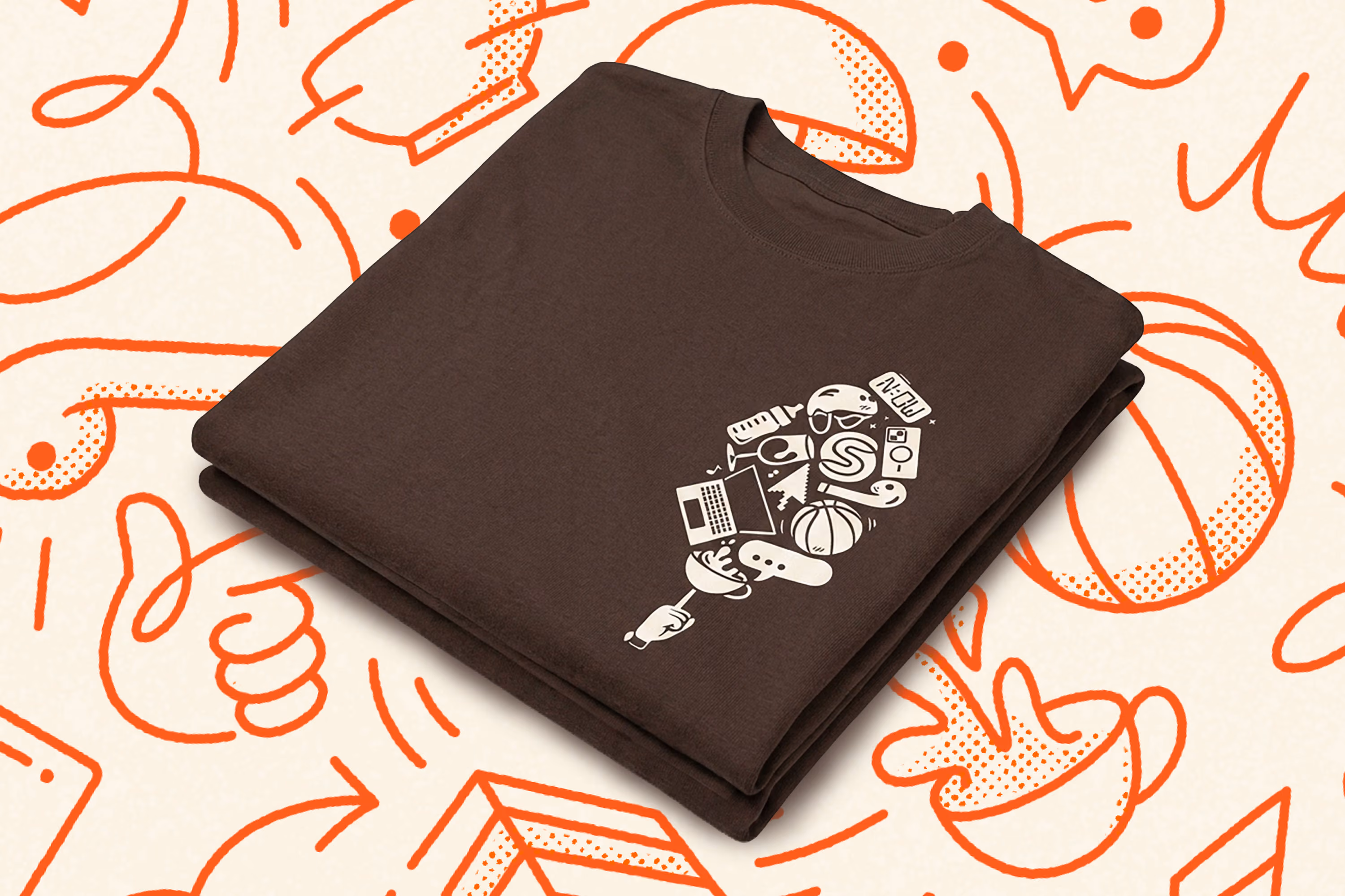 Folded dark brown T-shirt with a white graphic on the front featuring various icons including a basketball, laptop, game controller, camera, and music notes, arranged in a speech bubble shape, placed on a white surface with orange abstract illustrations.