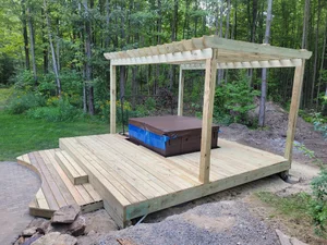 Wooden pergola on a raised cedar platform with a hot tub underneath, surrounded by trees in Weston Wisconsin