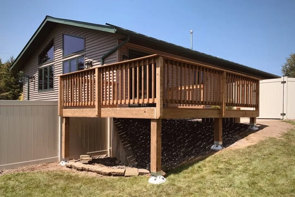 Elevated wooden deck attached to a beige Wausau home with a sloped green roof and fenced backyard