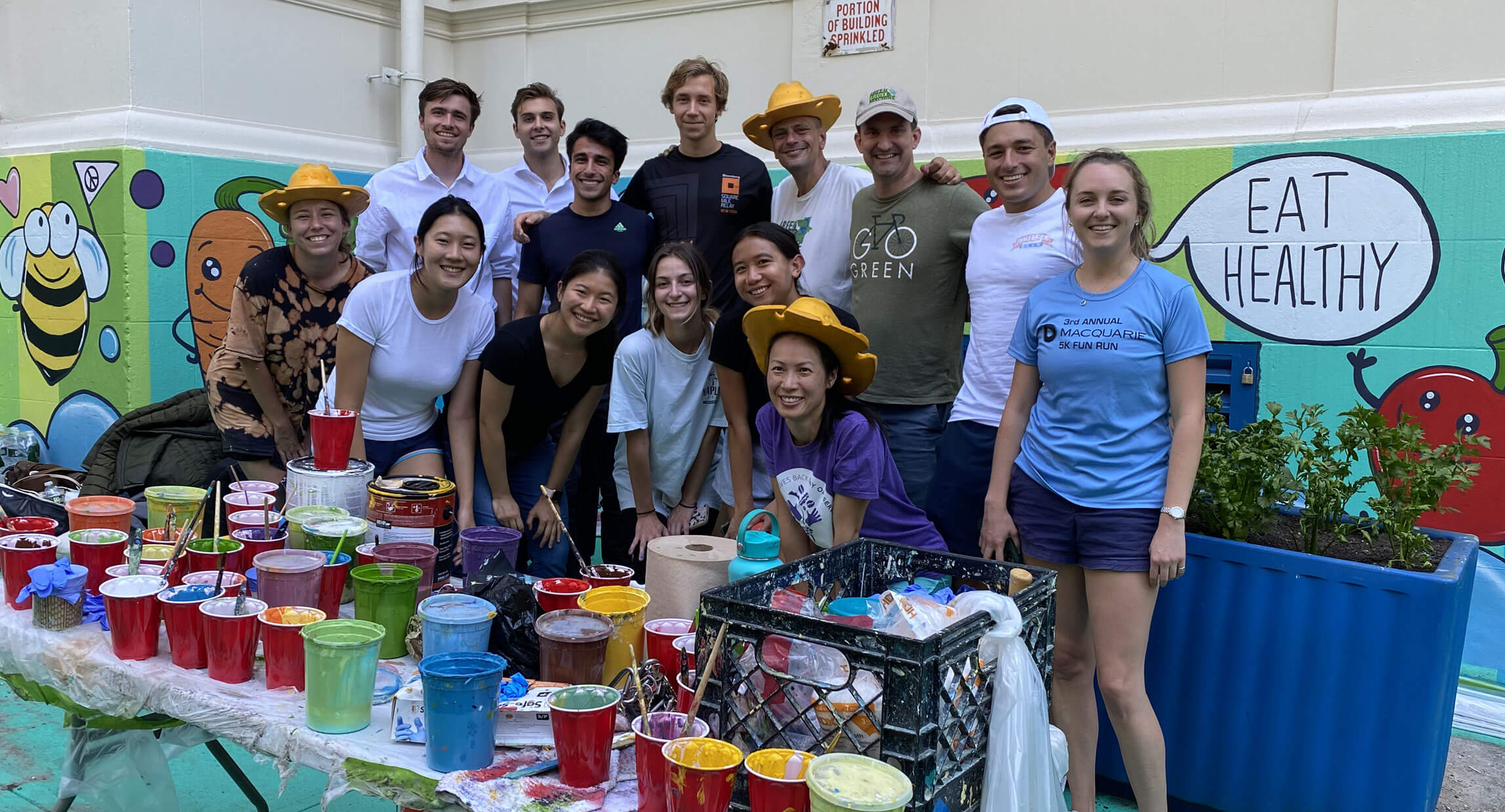 Volunteers gathered behind a table of paint supplies in front of a colorful garden mural