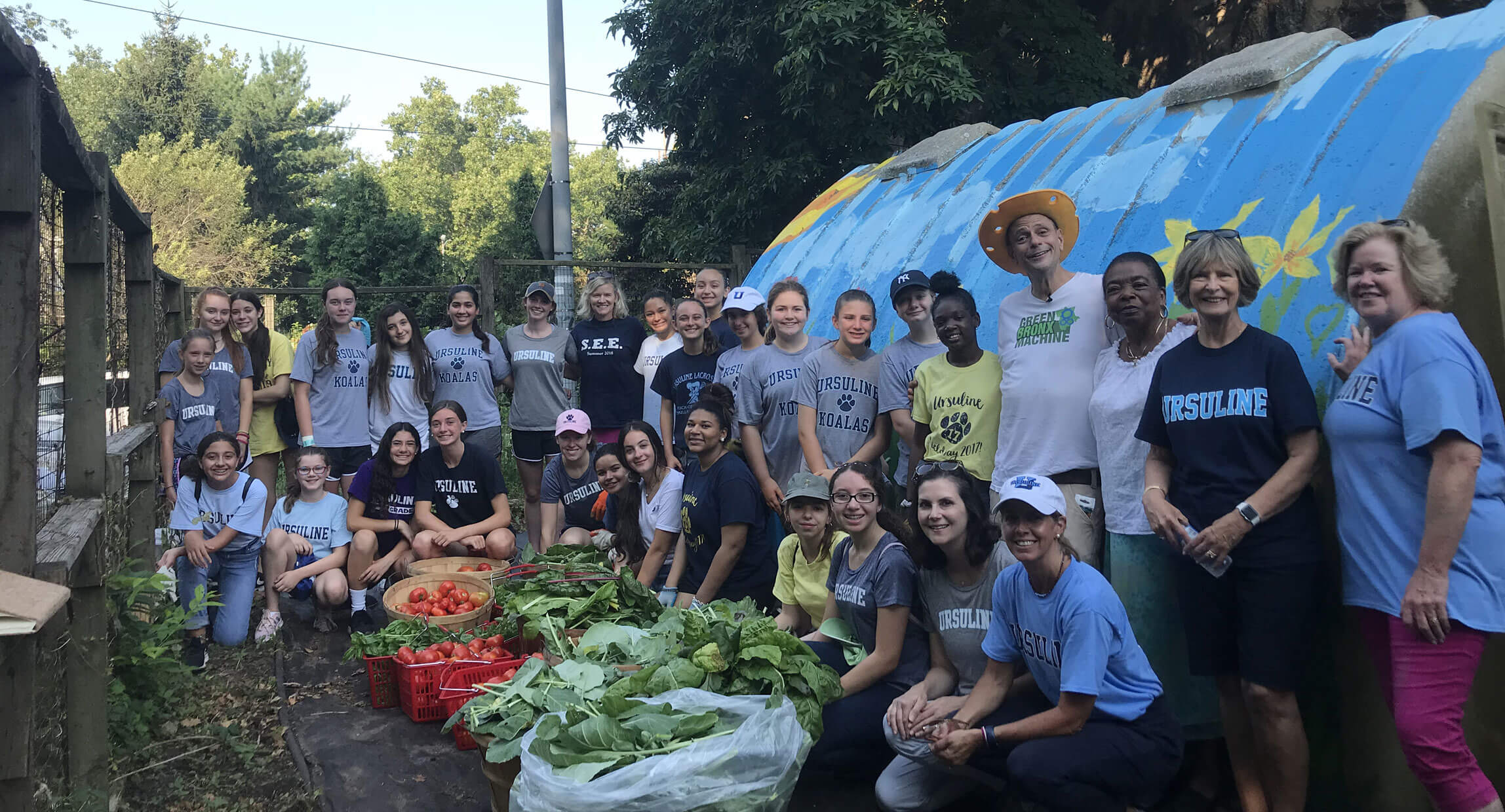 A large group of student volunteers behind a harvest of greens and tomatoes at a community garden