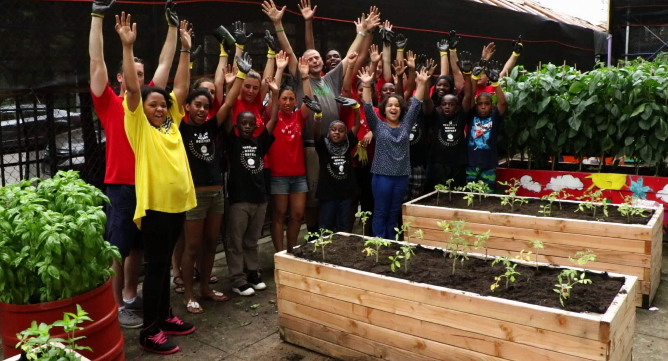 Students and volunteers cheering with raised arms beside raised planting beds