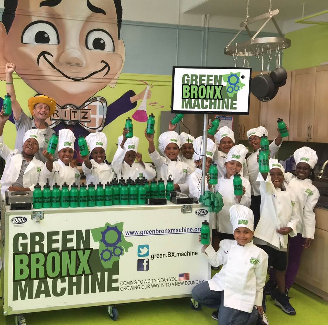 Students in a classroom holding trays of freshly harvested greens beside a Tower Garden