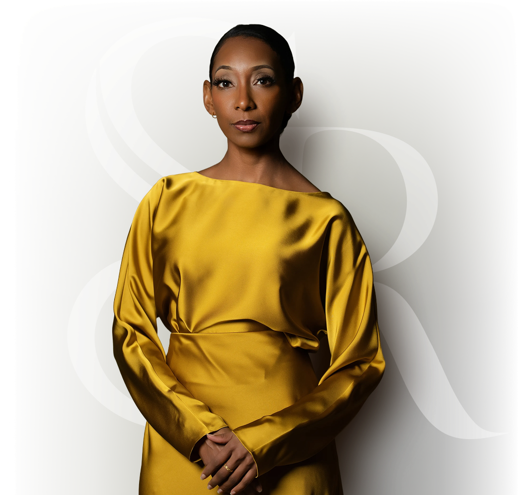 Woman with slicked-back hair wearing a shiny golden long-sleeve dress standing against a blurred background with white decorative letters.