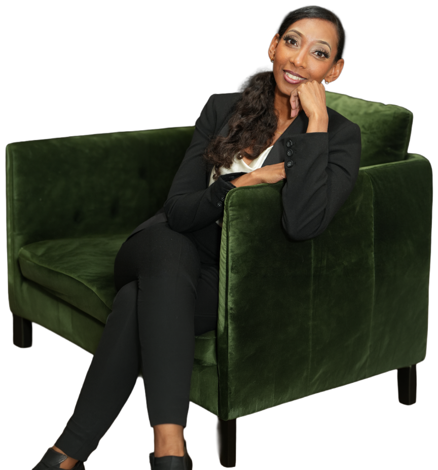 Woman with long dark hair wearing a black suit sitting on a green velvet armchair, resting her head on her hand and smiling.