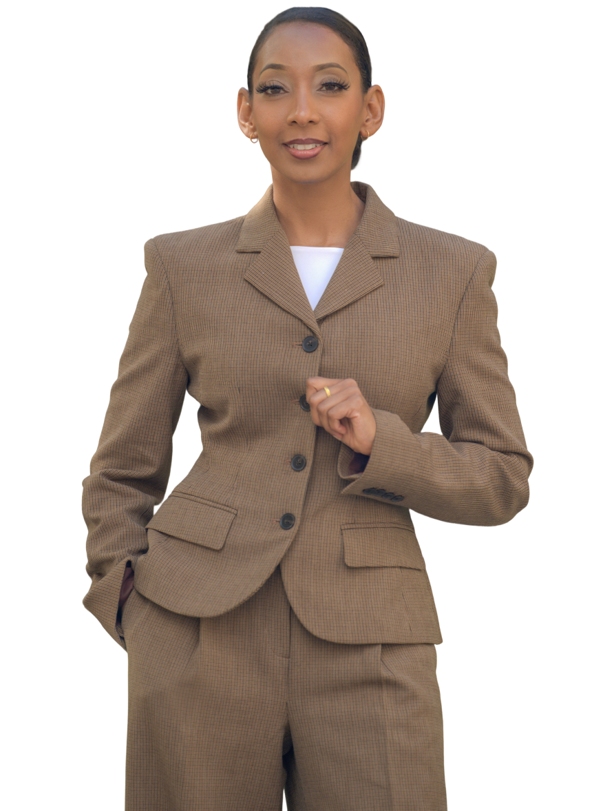 Woman wearing a brown checkered suit with a white top underneath, posing with one hand in pocket and the other adjusting the suit jacket.