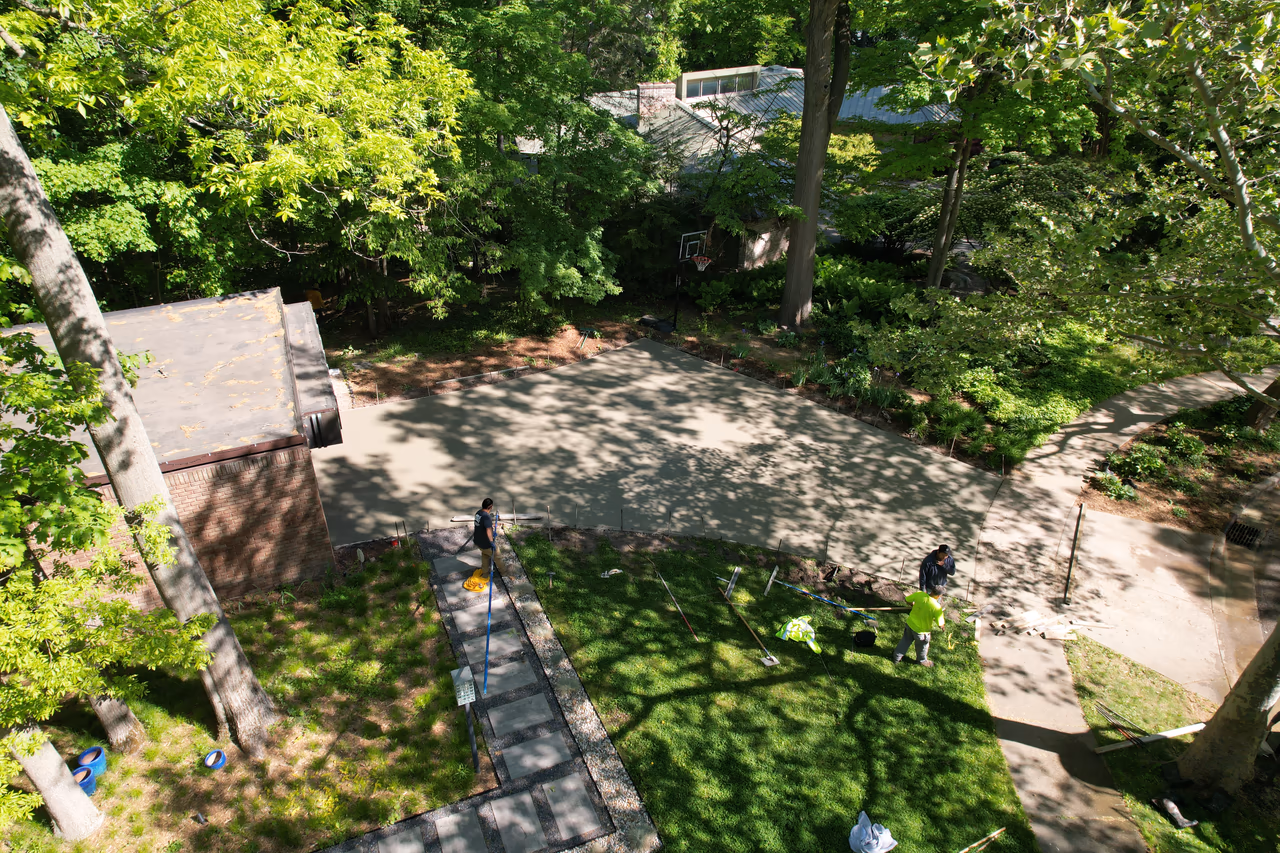 Aerial drone view of freshly poured concrete driveway pad with crew finishing edges