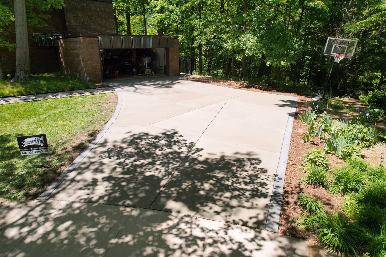 Completed modern concrete driveway with curved apron and Pro Concrete Services yard sign, Grand Rapids MI