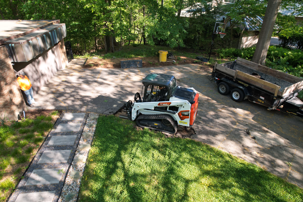 Bobcat skid steer removing old driveway surface during concrete demo, Grand Rapids MI