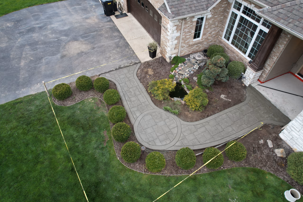 Aerial view of a curved stamped concrete walkway with decorative circle medallion winding through front yard landscaping in Caledonia MI
