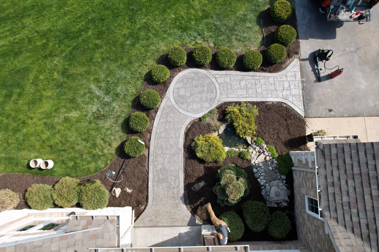 Overhead drone shot of curved stamped concrete walkway and circle medallion detail with garden landscaping and crew working in Caledonia MI
