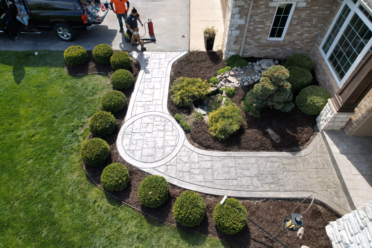 Close aerial view of stamped concrete walkway with decorative circle medallion and bordered edge detail surrounded by boxwood shrubs in Caledonia MI
