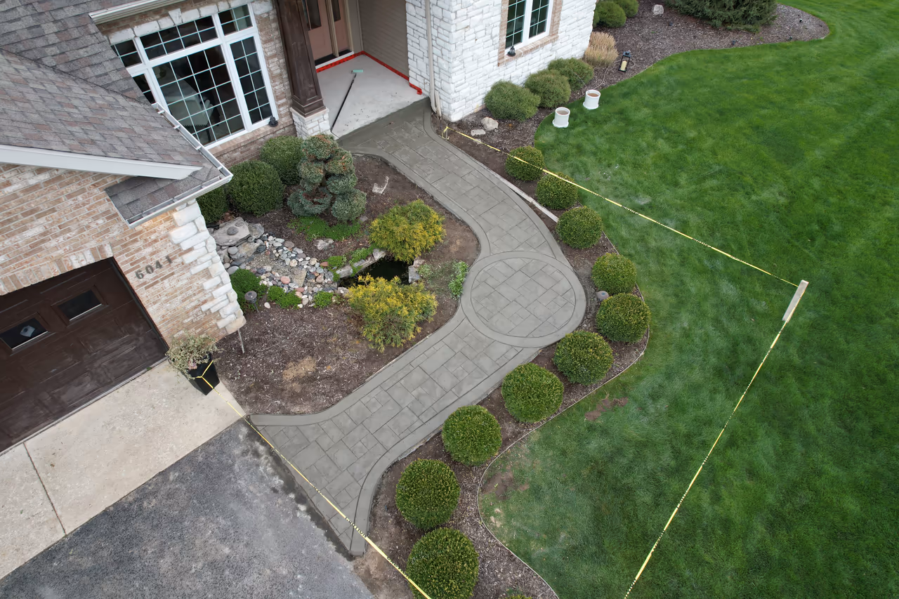 Drone shot of a curved stamped concrete walkway with circle medallion detail surrounded by manicured shrubs and garden beds in Caledonia MI