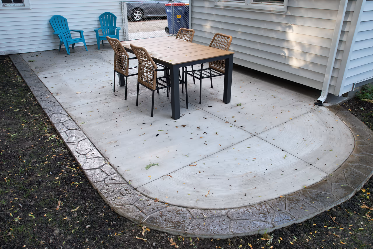 Completed broom finish backyard patio with stamped decorative border and outdoor dining set in Grand Rapids MI