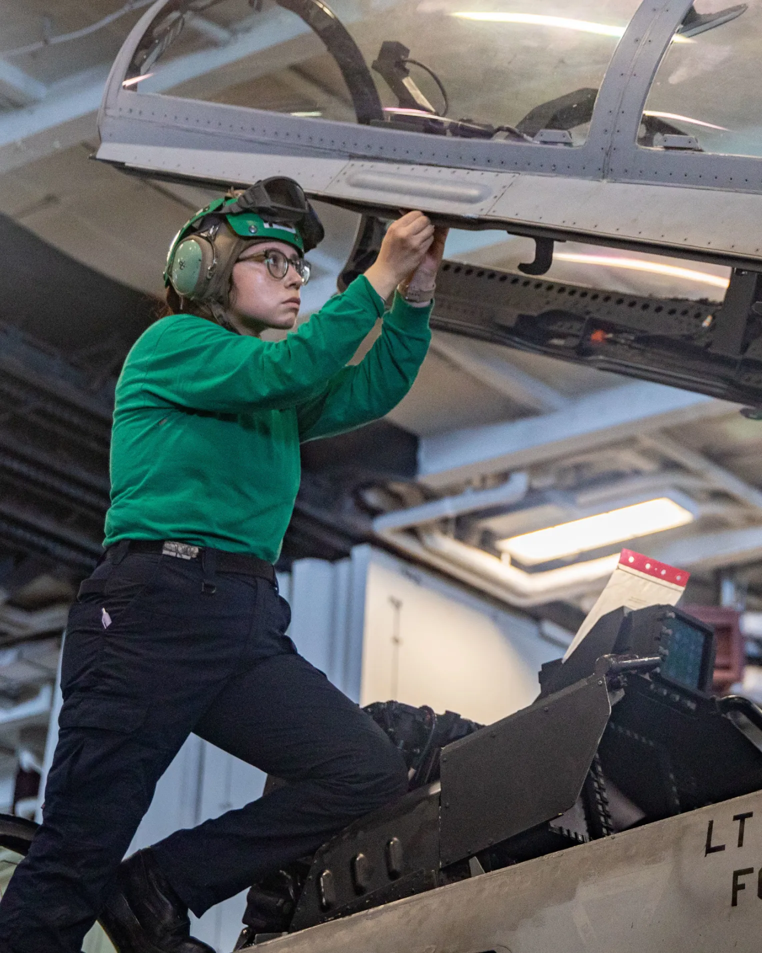 a woman wearing green shirt and goggles working on a plane