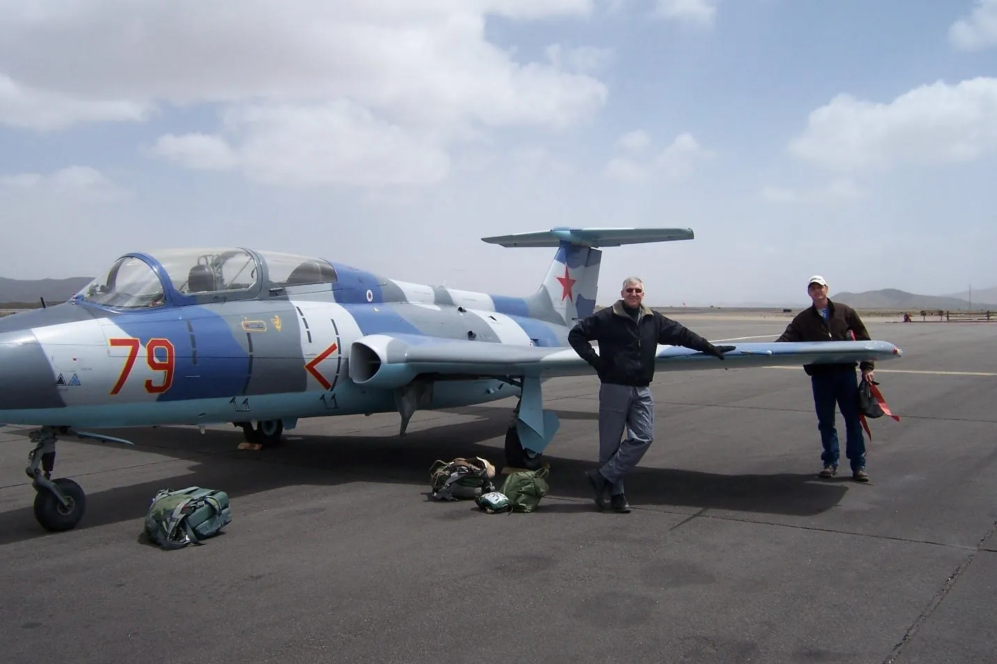 L-29 aircraft in on tarmac with flight crew leaning on wing