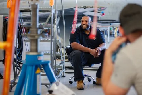 Smiling mechanic seated beneath aircraft