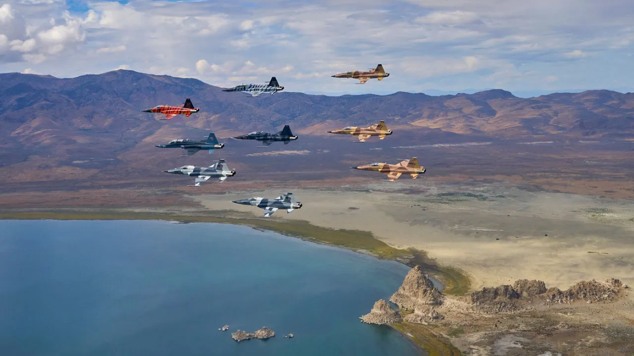 Fleet of Tactical Air Support F5s flying in formation over lake