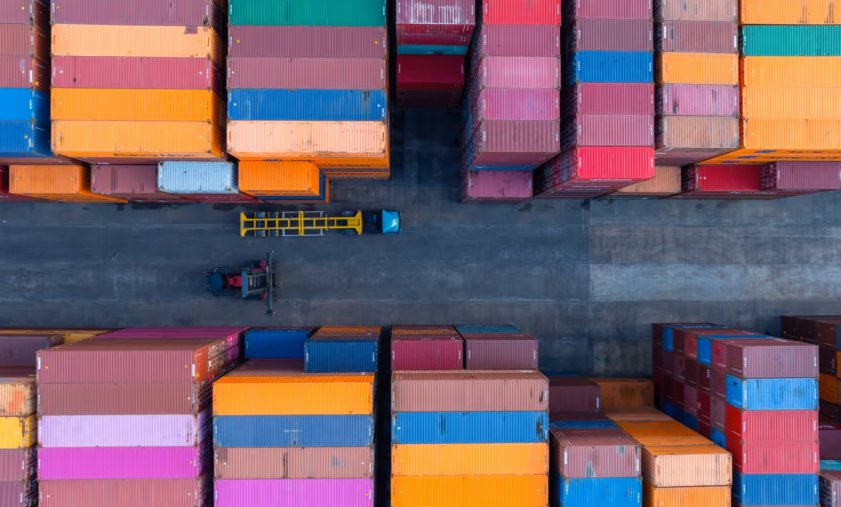 Luftaufnahme eines verkehrsfreien Containerterminals mit bunten Frachtcontainern und Gabelstaplern.