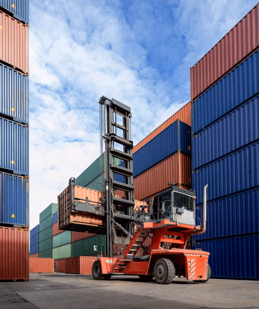 Roter Gabelstapler hebt einen Container in einem Lager mit gestapelten bunten Frachtcontainern.