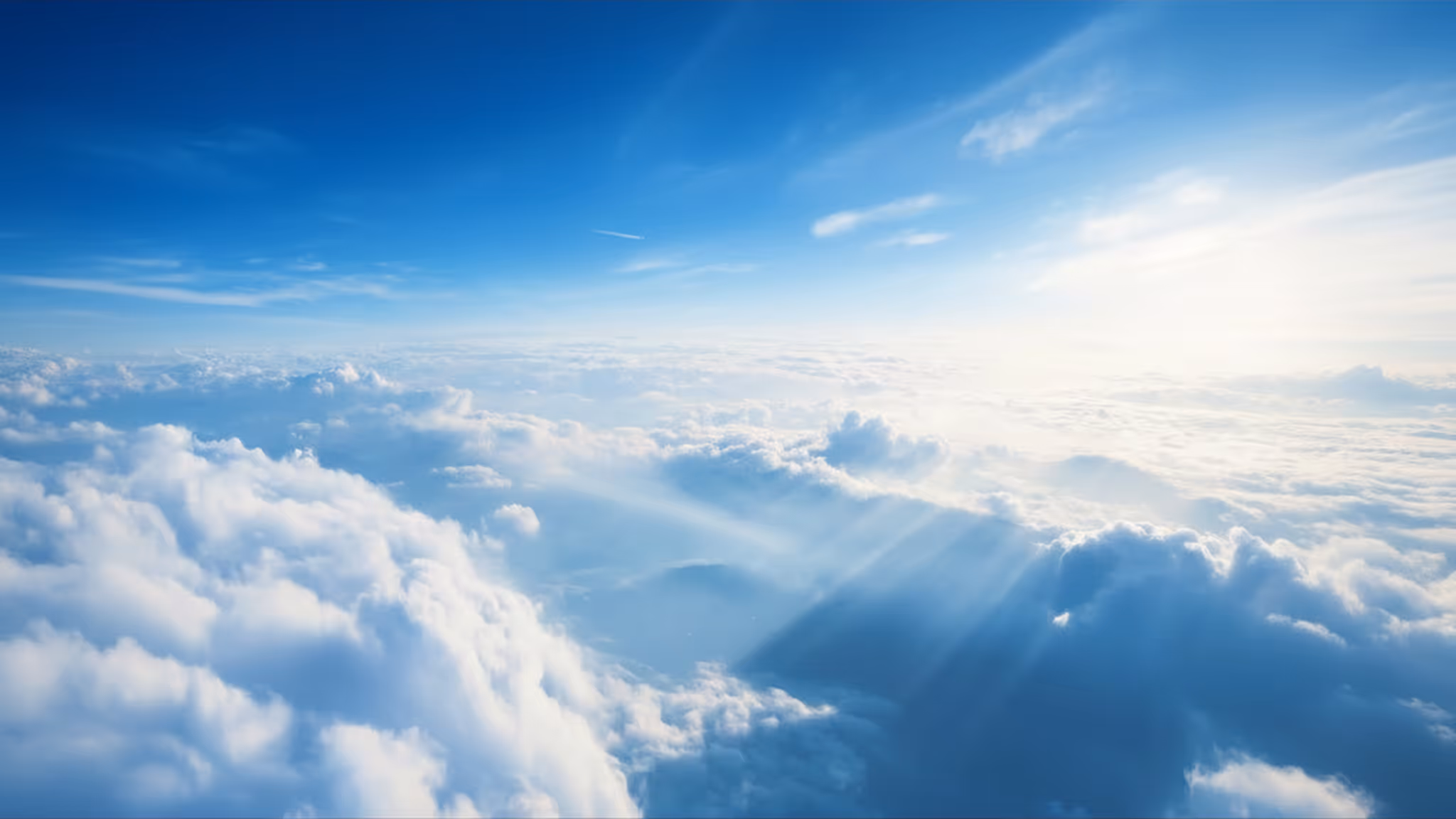 Sonnenstrahlen scheinen durch weiße Wolken unter blauem Himmel.