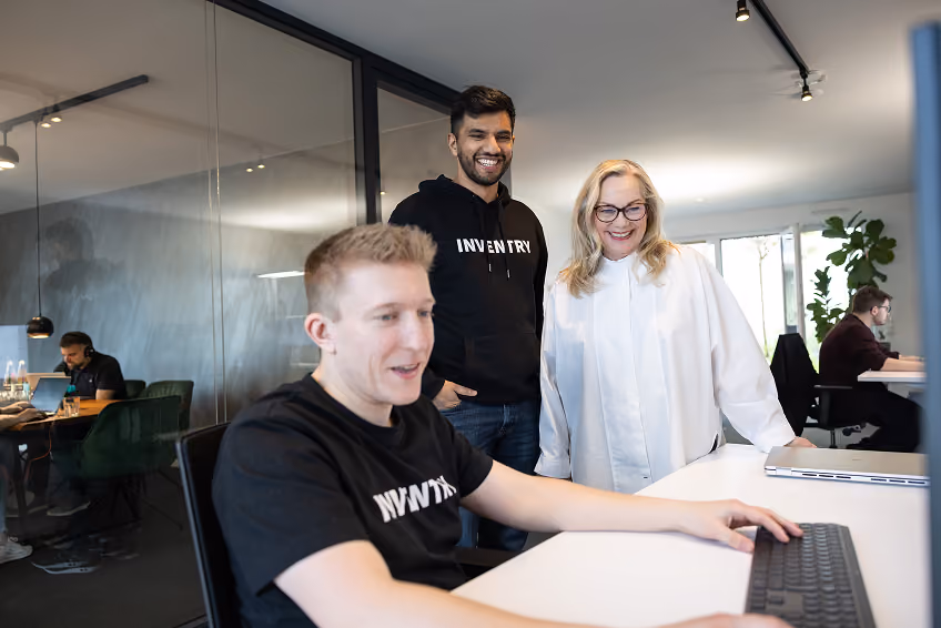 Drei lächelnde Kollegen in einem modernen Büro arbeiten gemeinsam an einem Computer.
