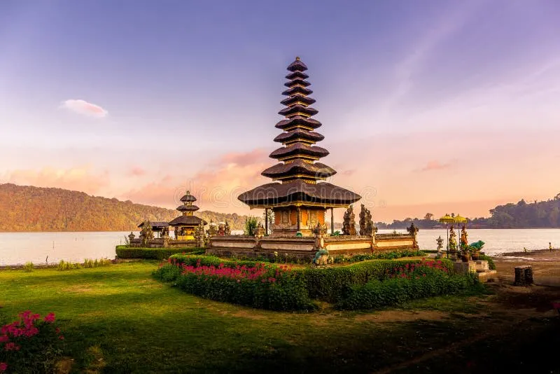 Traditional multi-tiered Balinese temple near a lake with mountains under a purple sunset sky.