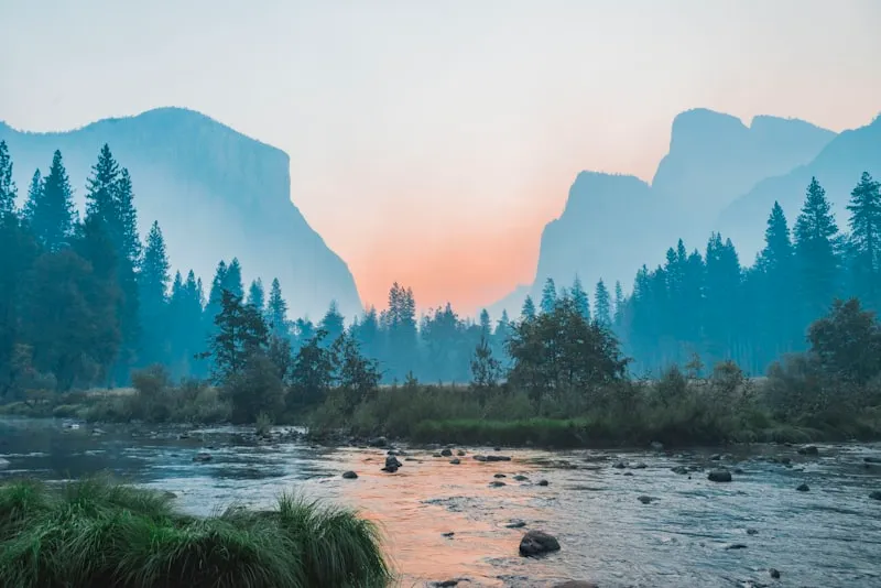 River flowing through forested valley with mountains in fog at sunrise or sunset.
