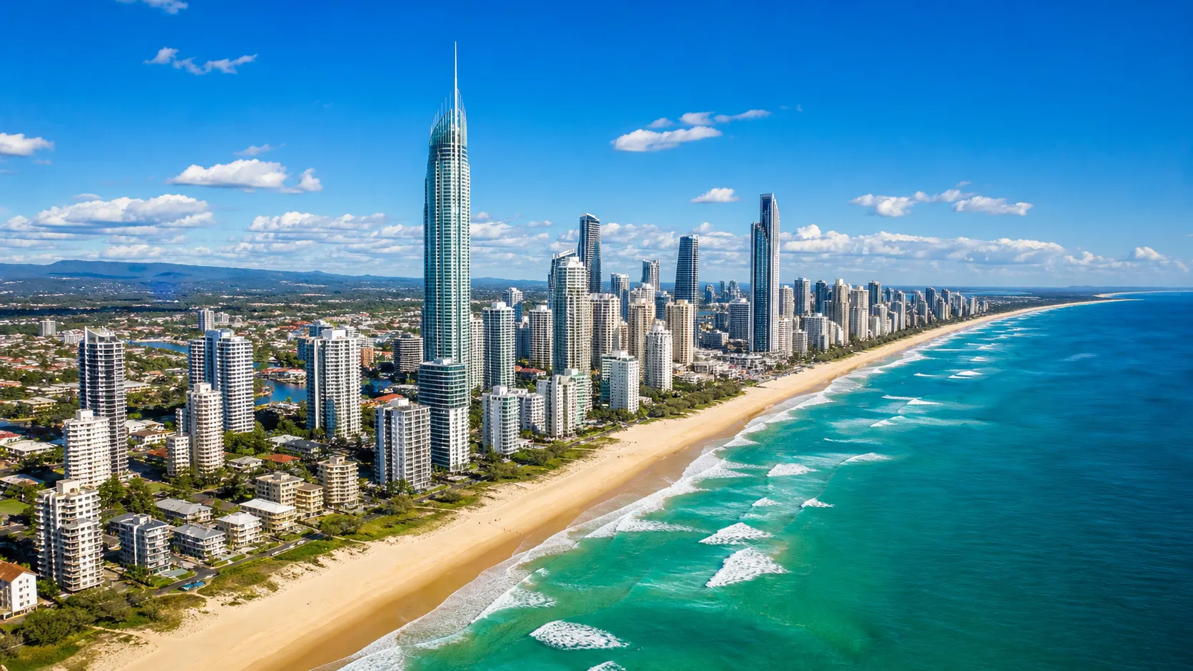 Aerial view of a city skyline with tall skyscrapers along a sandy beach and blue ocean waves.