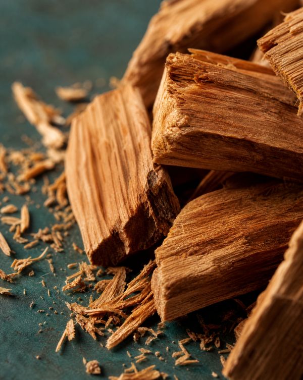 Close-up of rough, broken cedarwood pieces on a green surface with wood shavings scattered around.