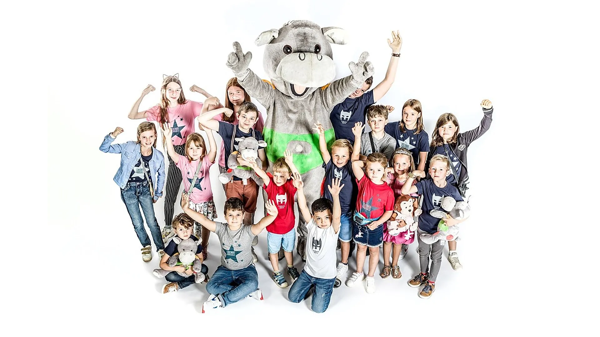 Een groep lachende kinderen steekt de armen in de lucht rond Hippo, de nijlpaardmascotte van Hippo and Friends.