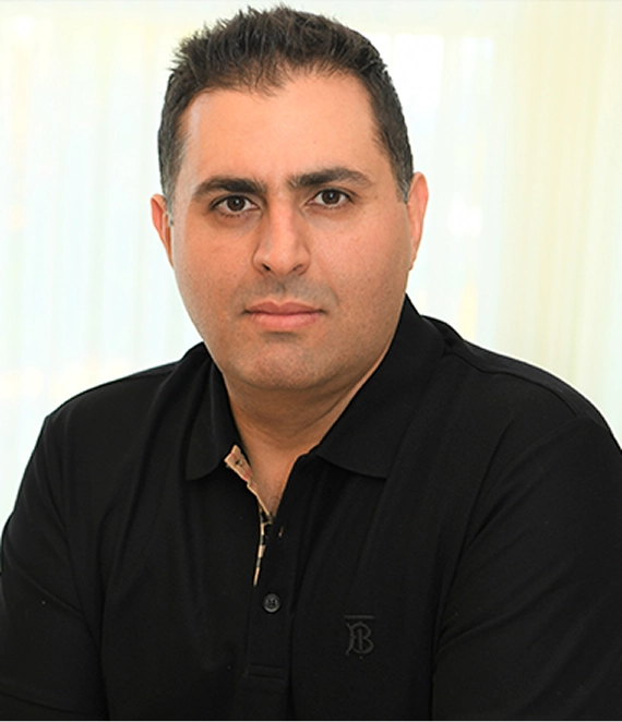 Man with short dark hair wearing a black collared shirt, looking directly at the camera.
