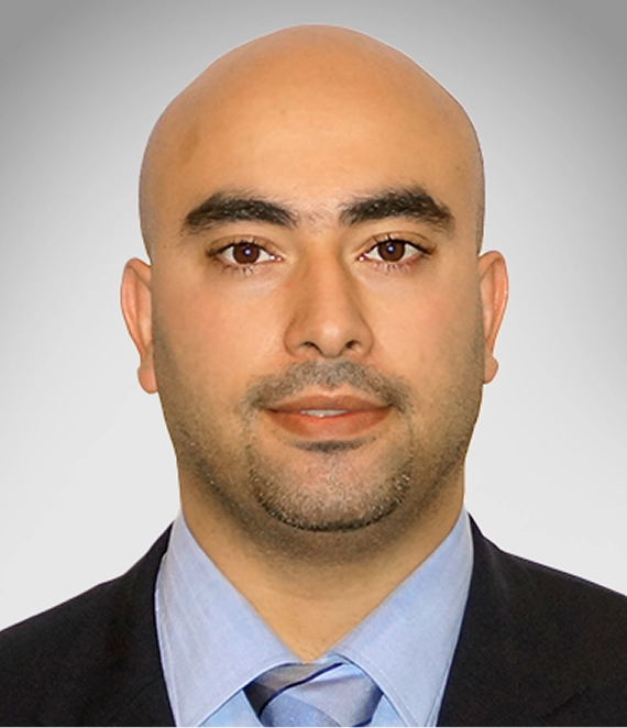 Portrait of a bald man with trimmed beard wearing a suit, light blue shirt, and striped blue tie.