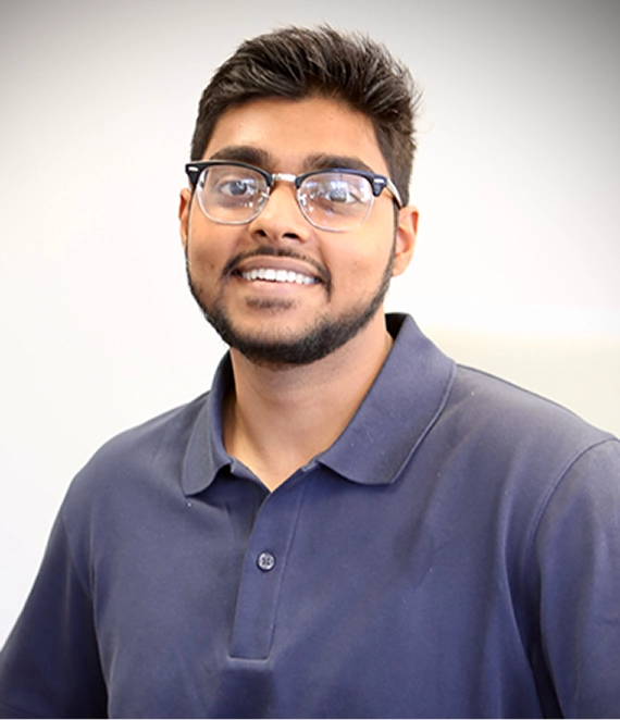 Smiling young man with glasses and a beard wearing a navy blue collared shirt.