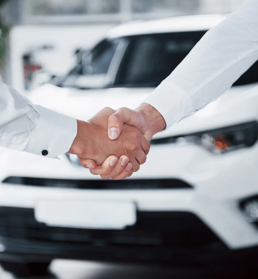 Two people shaking hands in front of a white car, symbolizing a car deal or agreement.
