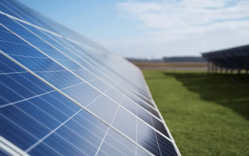 Close-up of blue solar panels installed in a field under a partly cloudy sky.