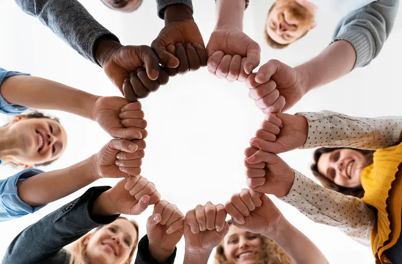 A diverse group of people forming a circle with their fists joined in the center.