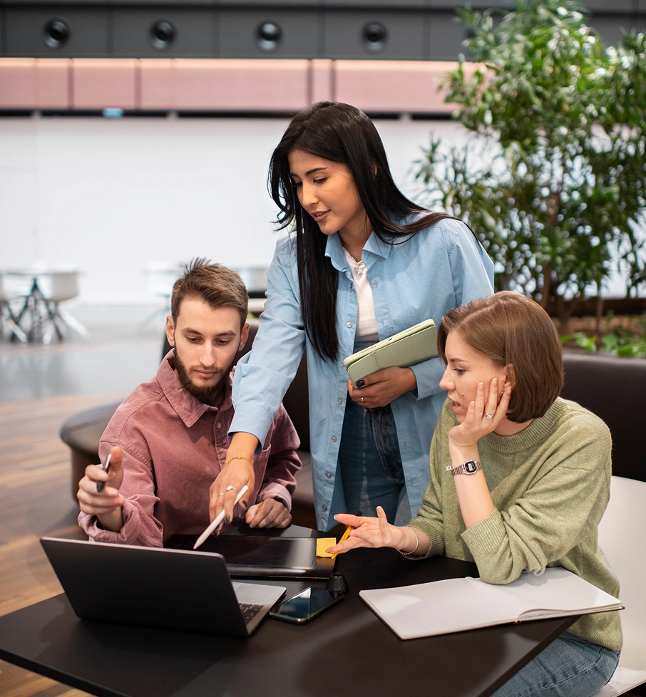 Three people collaborating around a laptop, pointing at the screen in a modern office space.