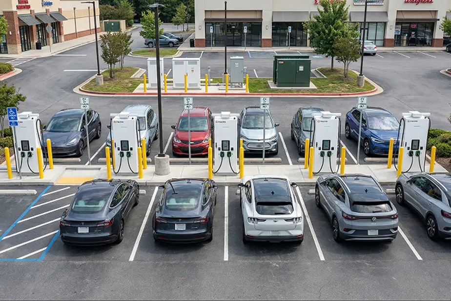 Electric vehicles parked and charging at six charging stations in a commercial parking lot.