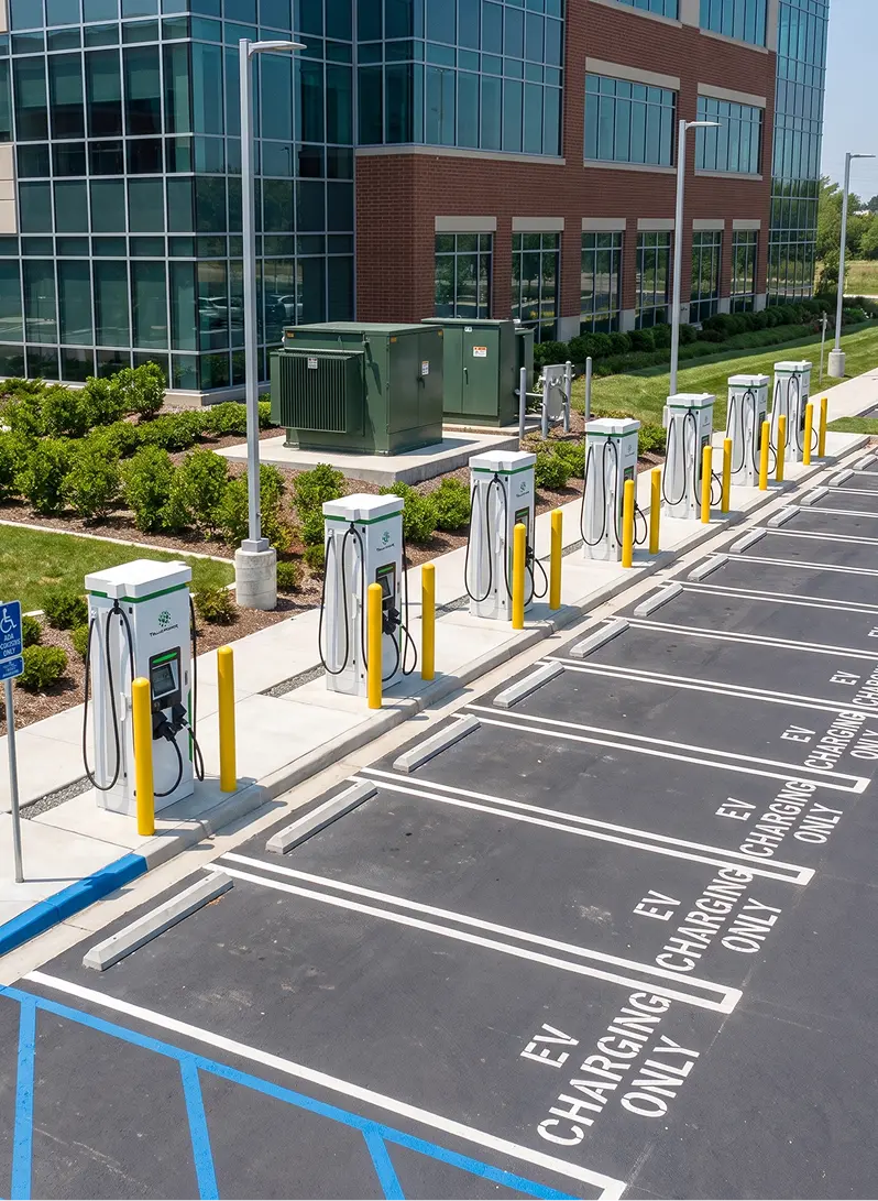 Row of electric vehicle charging stations in an empty parking lot next to a glass and brick building.