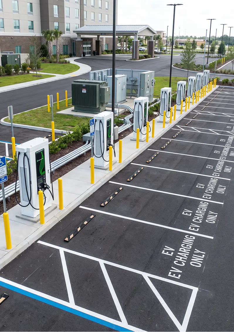 Row of electric vehicle charging stations in an empty parking lot next to a glass and brick building.