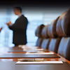 Close-up of a conference table with empty chairs and a blurred businessman in the background.