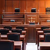Empty courtroom with wooden judge's bench, American flag, and rows of black chairs.